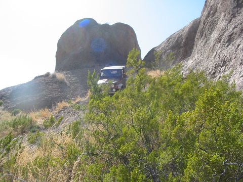 1996 Ford Bronco - A red Jeep Wrangler navigates a , rocky terrain with large boulders and sparse vegetation.