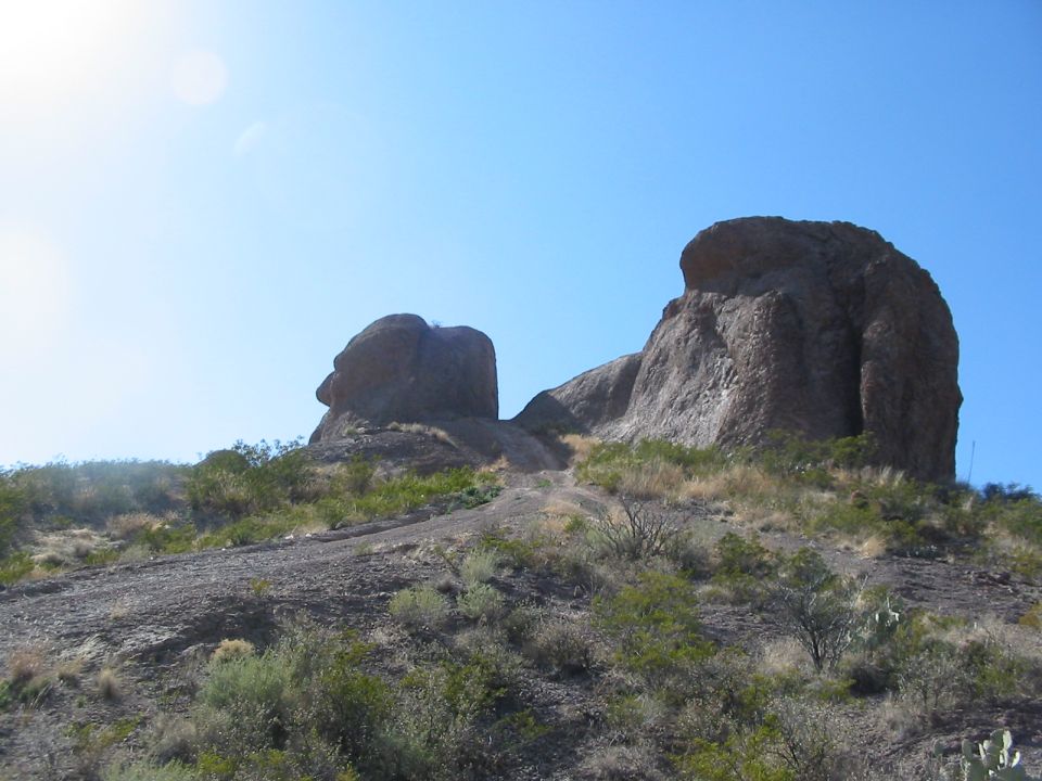 Large rock formations on a hill under a clear blue sky. A dirt path leads up between them