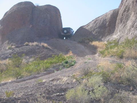 1996 Ford Bronco - An SUV navigates a challenging off-road trail through a rocky landscape under a clear sky.