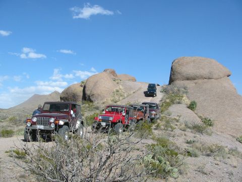 1996 Ford Bronco - A convoy of Jeep Wranglers navigates a desert landscape under a clear blue sky.