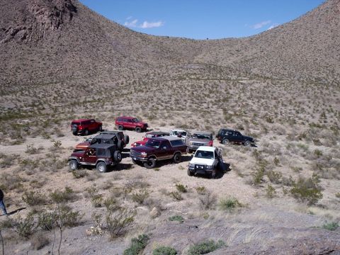 1996 Ford Bronco - A collection of SUVs and trucks are gathered in a dry, arid landscape under a clear blue sky.