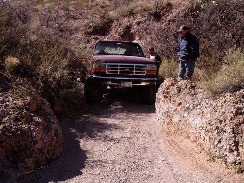 1996 Ford Bronco - Ford F-Series truck navigates a narrow, rocky trail in a desert landscape.