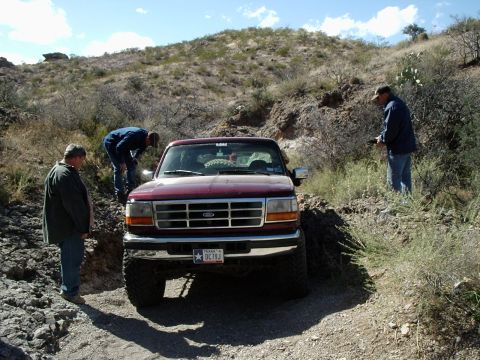 1996 Ford Bronco - A red 1995 Ford Bronco navigates a rough, off-road path with three men observing.