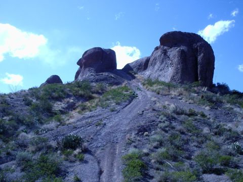 1996 Ford Bronco - A dirt path winds up a rocky incline towards imposing rock formations under a bright blue sky.