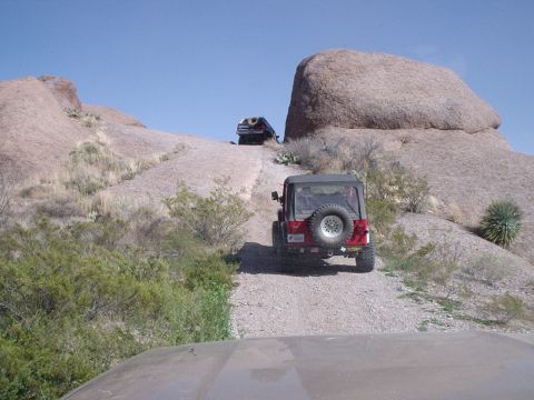 1996 Ford Bronco - Two Jeep Wranglers navigate a challenging off-road trail through a rocky, arid landscape.