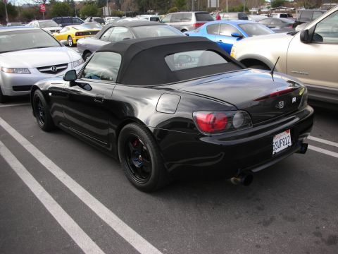 1998 Ford Crown Victoria - Rear three-quarter of a black Honda S2000 roadster with its soft top up and black wheels, parked among cars at a meet.