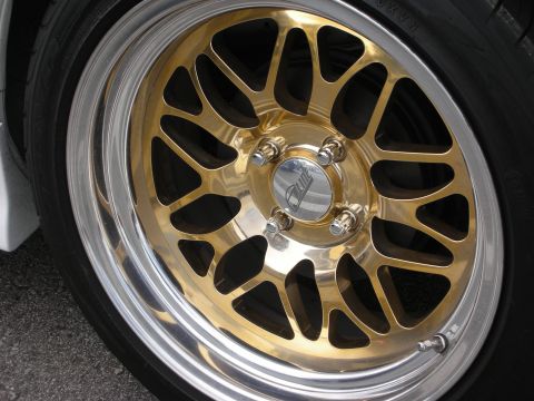 1998 Ford Crown Victoria - Close-up of a gold mesh-pattern aftermarket wheel with a polished outer lip and chrome lug nuts mounted on a white car.