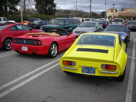 1998 Ford Crown Victoria - red Ferrari with a tan top sits beside a yellow vintage fastback coupe in a parking lot, with a McDonald's sign behind.