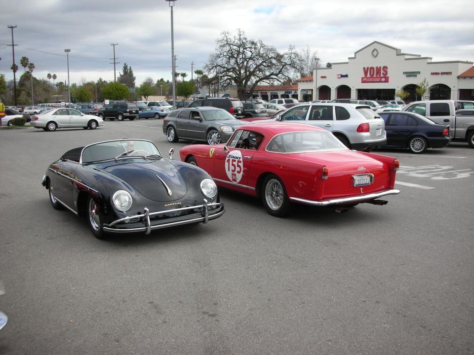 Black Porsche 356 Speedster beside red Ferrari coupe number 155 in lot