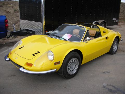 1998 Ford Crown Victoria - yellow Ferrari Dino 246 GTS targa with tan interior parked in front of an enclosed black trailer.