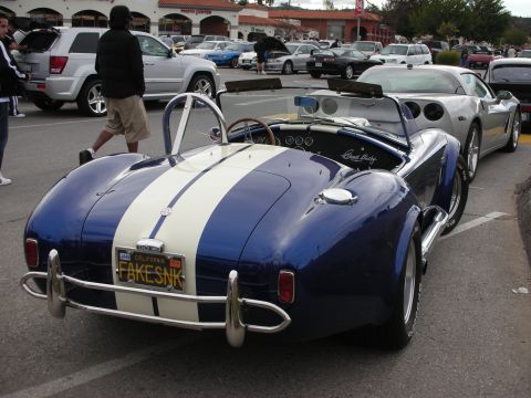 1998 Ford Crown Victoria - blue Shelby Cobra replica with white stripes seen from the rear, its California plate reading FAKESNK, beside a silver Corvette.