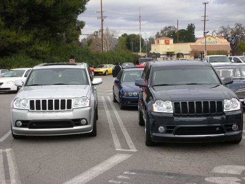 1998 Ford Crown Victoria - silver and a black Jeep Grand Cherokee SRT8 SUV parked facing the camera, with a McDonald's restaurant behind.