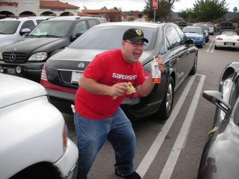 1998 Ford Crown Victoria - man in a red Sarcastic t-shirt holding food gives a thumbs up beside a black Maybach in a parking lot.