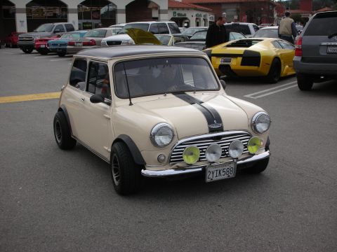 1998 Ford Crown Victoria - cream classic Mini Cooper with a black racing stripe, flared arches, and front driving lamps, parked near a yellow Lamborghini.