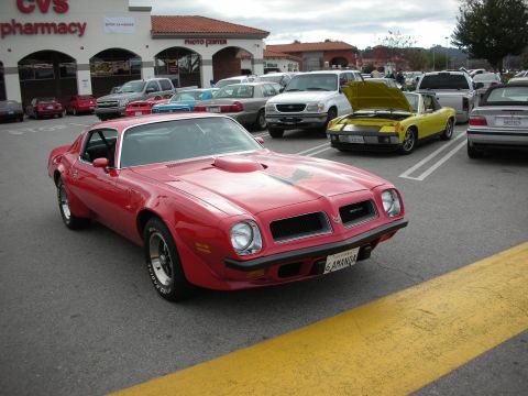 1998 Ford Crown Victoria - red Pontiac Firebird Trans Am with its hood bird decal, parked in a lot outside a CVS pharmacy.