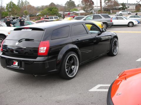 1998 Ford Crown Victoria - black Dodge Magnum wagon sits lowered on dark multi-spoke wheels in a crowded car-show parking lot.