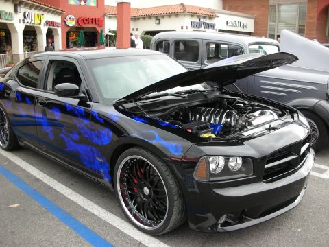 1998 Ford Crown Victoria - black Dodge Charger with blue flame graphics and large black wheels sits with its hood open outside shops.
