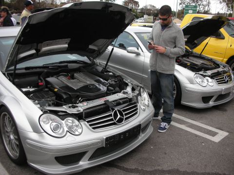 1998 Ford Crown Victoria - silver Mercedes-Benz CLK sits with its hood open as a man checks his phone beside more cars at a meet.