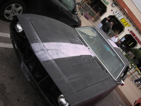 1998 Ford Crown Victoria - black muscle car finished in matte primer with a light stripe sits outside a Subway shop, high-angle view.