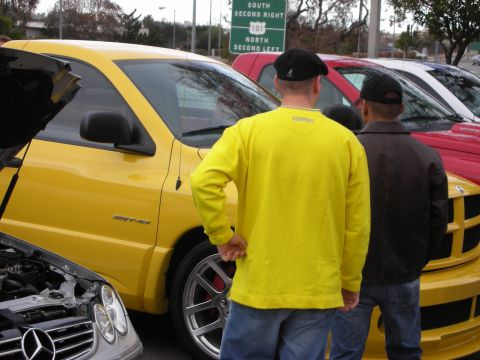 1998 Ford Crown Victoria - Two men stand looking at a yellow Dodge Ram SRT-10 and a red truck beside a freeway sign at a car meet.