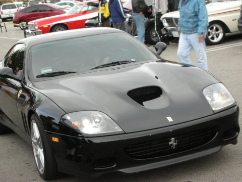 1998 Ford Crown Victoria - black Ferrari coupe with a center hood vent and Ferrari badge sits at a crowded outdoor car show.