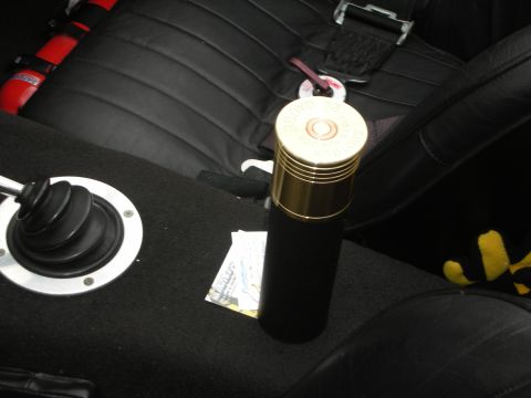 1998 Ford Crown Victoria - brass shotgun-shell-style canister stands on a black leather console near a shifter boot and red racing harness.