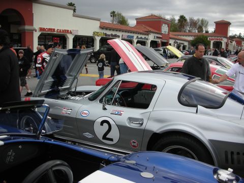 1998 Ford Crown Victoria - silver vintage Corvette race car wearing number 2 sits with hood raised among cars at a strip-mall car show.