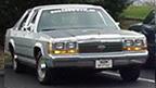 1989 Ford LTD Crown Victoria - Front three-quarter view of a silver Ford full-size sedan parked outdoors, showing its chrome grille, dual rectangular headlights, and Ford…