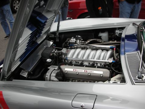 1998 Ford Crown Victoria - polished V8 engine with Grand Sport-stamped valve covers sits in the bay of a silver and blue sports car.