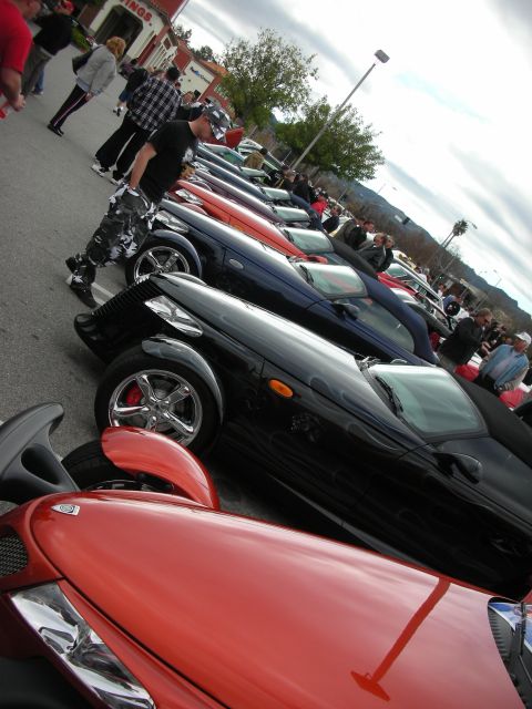 1998 Ford Crown Victoria - line of Plymouth Prowler roadsters in red and black recedes along a parking lot under a cloudy sky.
