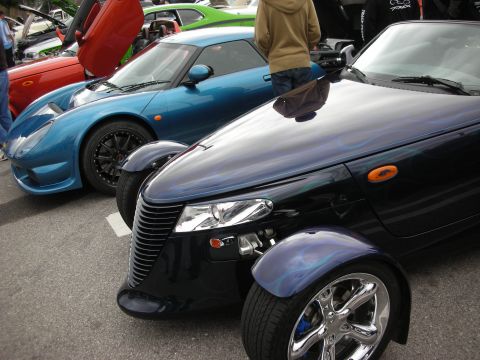 1998 Ford Crown Victoria - Front quarter of a dark purple Plymouth Prowler with chrome wheels parked beside a blue sports car at a show.