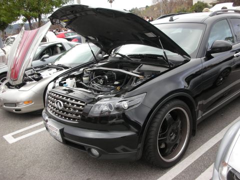1998 Ford Crown Victoria - black Infiniti FX crossover with raised hood and dark aftermarket wheels parked at an outdoor car show.