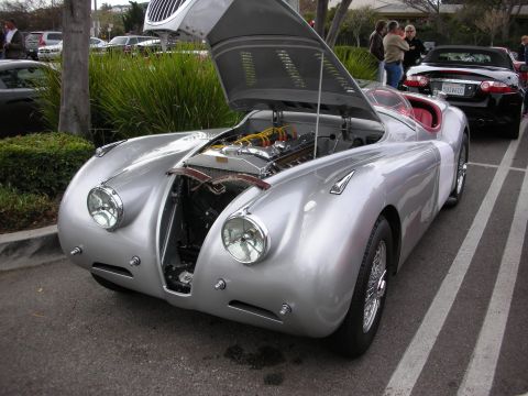 1998 Ford Crown Victoria - silver Jaguar XK-style roadster with hood raised exposes its inline engine, parked at an outdoor car show.