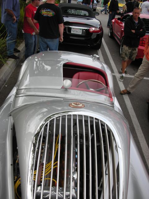 1998 Ford Crown Victoria - silver classic British sports roadster with a chrome vertical-slat grille and red interior sits among other cars at an outdoor show.