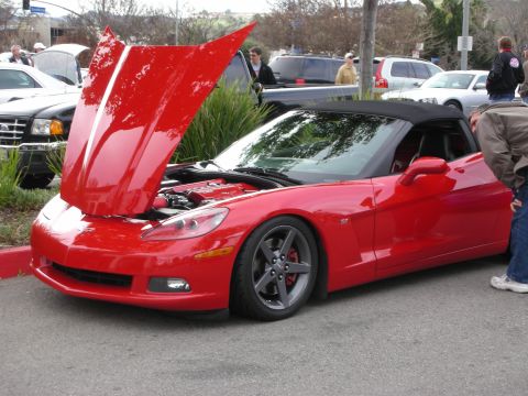 1998 Ford Crown Victoria - red Chevrolet Corvette convertible displayed with its clamshell hood raised and top up at an outdoor car gathering.