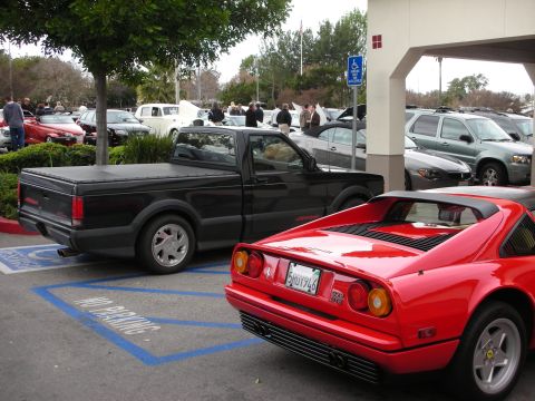 1998 Ford Crown Victoria - black sport pickup truck parked beside a red Ferrari coupe with pop-up headlights in a paved show lot.