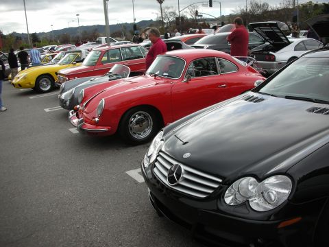 1998 Ford Crown Victoria - lineup of classic sports cars including a red Porsche 356 coupe and a black Mercedes, with spectators on a cloudy day.
