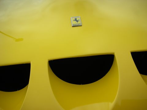 1998 Ford Crown Victoria - Close-up of a yellow Ferrari front hood showing the prancing-horse badge above half-moon air vents.