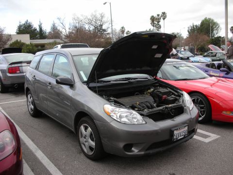 1998 Ford Crown Victoria - gray Toyota Matrix wagon with its hood raised parked next to a red roadster in a tree-lined show lot.
