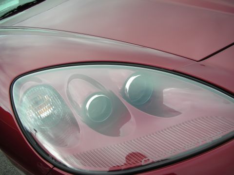 1998 Ford Crown Victoria - Close-up of a red sports car's clear headlight cluster showing three projector lamps under a smooth lens.