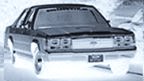 1989 Ford LTD Crown Victoria - Front three-quarter view of a dark-colored 1980s Ford full-size sedan photographed in a snowy outdoor setting, with a visible chrome grille…
