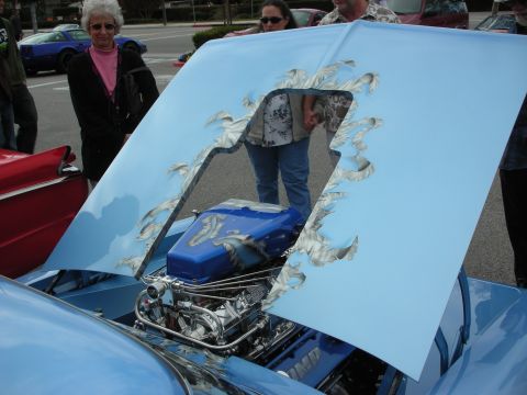 1998 Ford Crown Victoria - light blue custom car with airbrushed flame graphics on the raised hood revealing a chromed engine, with onlookers.