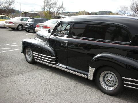 1998 Ford Crown Victoria - black 1940s Chevrolet sedan delivery panel truck with chrome fender skirts and trim parked in an asphalt lot.