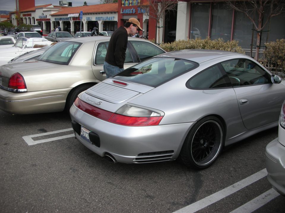 Silver Porsche 911 coupe parked behind a tan sedan at a strip mall