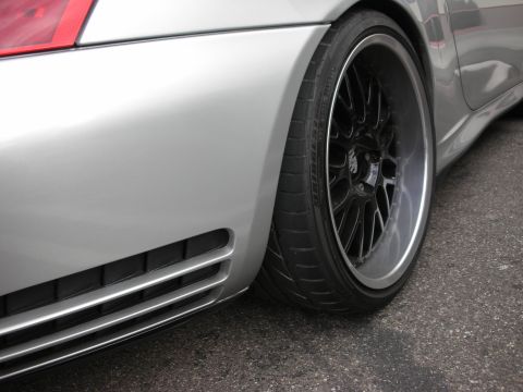 1998 Ford Crown Victoria - close-up of a silver Porsche's rear quarter panel, red taillight edge and black multi-spoke wheel with low-profile tire.