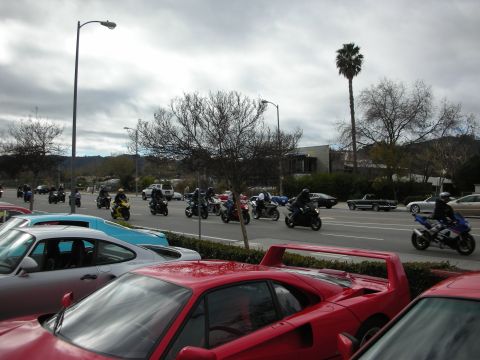1998 Ford Crown Victoria - group of motorcycles rides along a road past parked red and silver sports cars under a gray overcast sky.