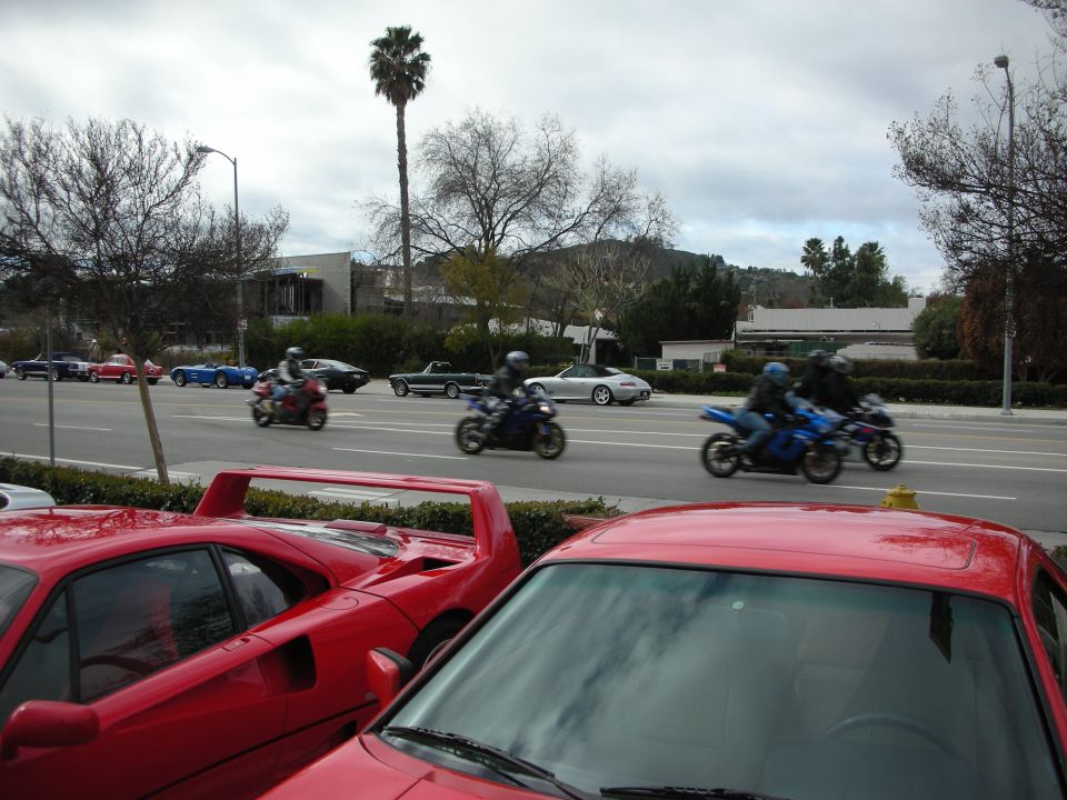 Blue and other motorcycles passing red sports cars on a road