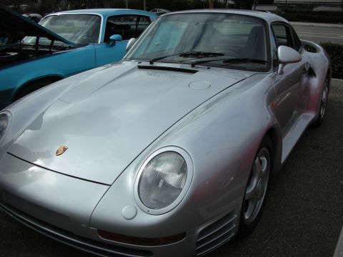 1998 Ford Crown Victoria - front of a silver Porsche 959 showing the crest, pop-up-style headlights and hood, parked beside a teal 911.
