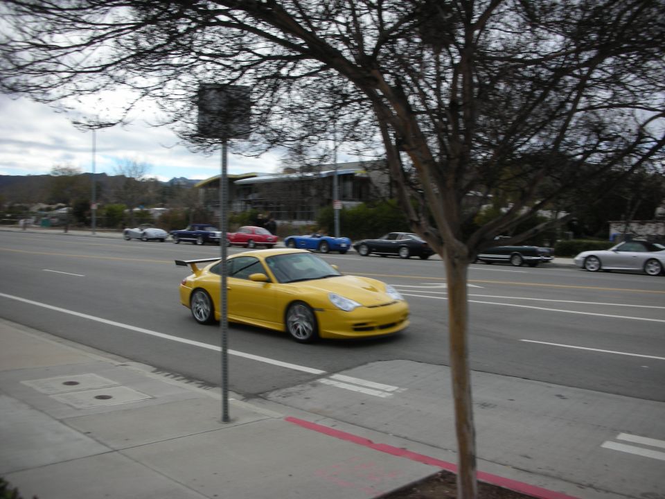 Yellow Porsche 911 GT3 with rear wing driving down a road