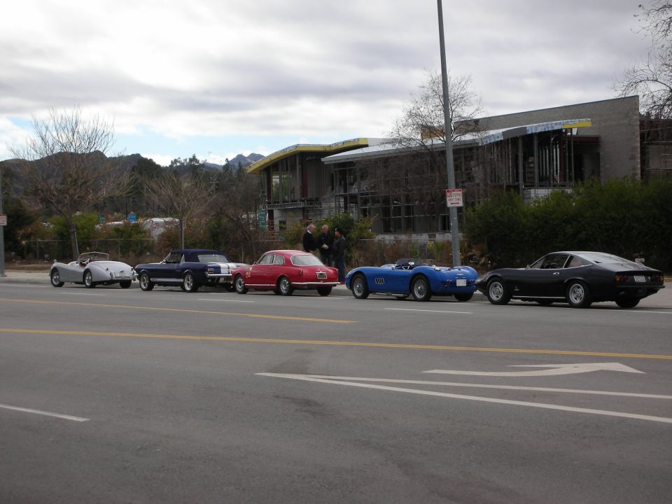 Row of vintage roadsters and a coupe parked along a roadside